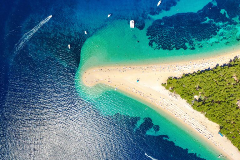 Aerial view of a beach on Brač Island with crystal-clear turquoise water and a small boat