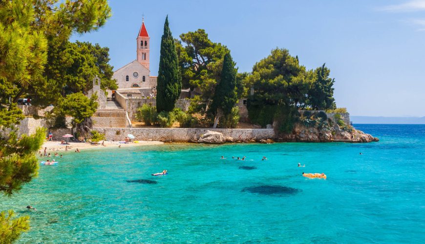 beach with clear blue water, old church, and green trees, Bol, Brač island (Dalmatia)