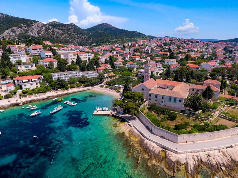 Aerial view of Hvar town with clear blue waters and boats in the harbor, surrounded by mountains