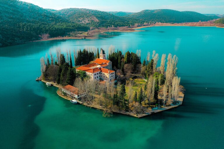 Aerial view of a small island surrounded by turquoise waters with lush greenery and buildings, Krka National Park
