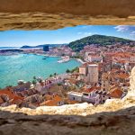 A scenic view from a stone window, showing the old town, harbor, and mountains in the background, Split