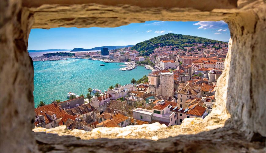 A scenic view from a stone window, showing the old town, harbor, and mountains in the background, Split