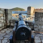 Old cannon on Dubrovnik's City Walls aimed over the Old Harbour at golden hour