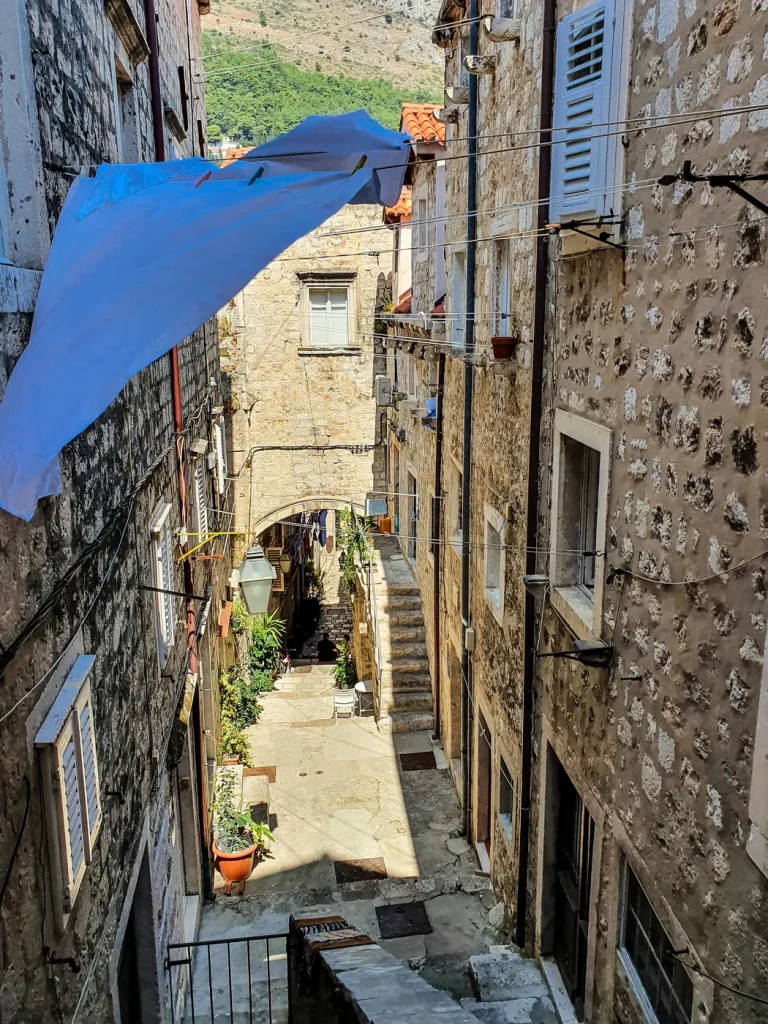 Steep narrow Dubrovnik Old Town street with stone stairs, laundry and a blue awning